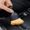 A hand is holding an ultra-soft curved detailing brush with a black handle and golden bristles, positioned near a car vent or