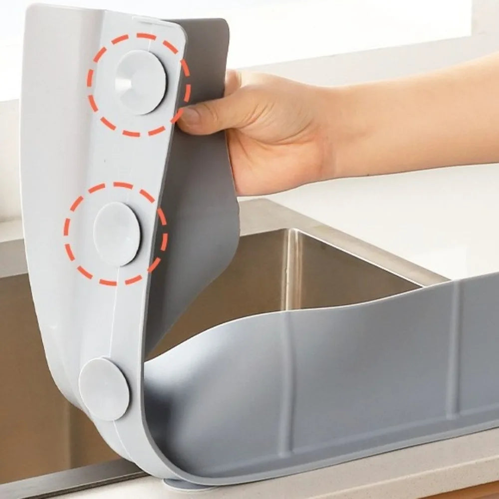 A hand is installing a flexible silicone sink splash guard with suction cups onto a kitchen sink.