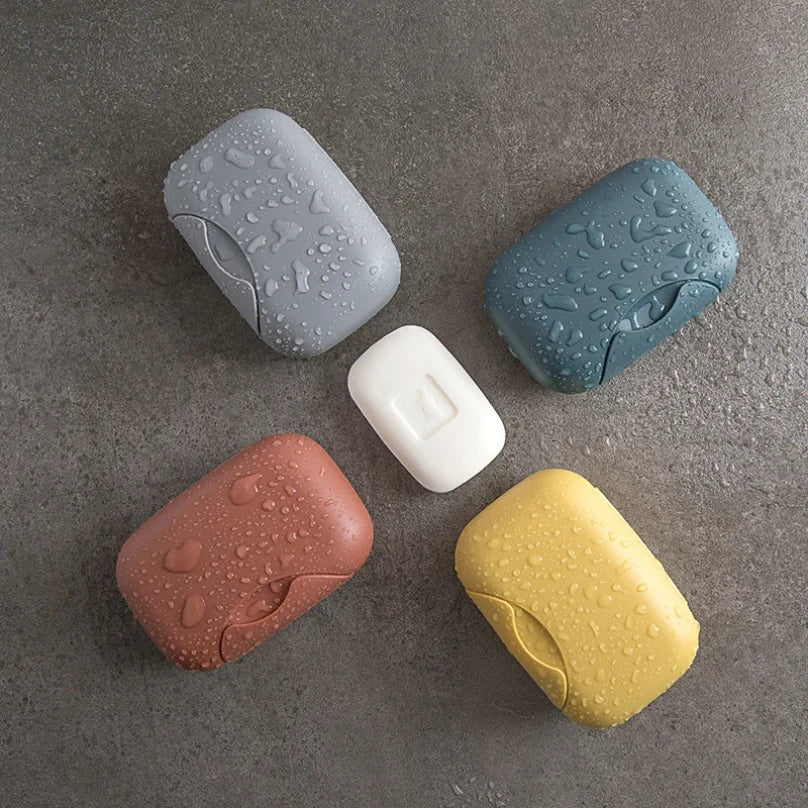 A collection of five leak-proof travel soap boxes in various colors including gray, blue, white, pink, and yellow on a gray s