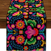 A vibrant floral pattern table runner featuring bright pink, purple, orange, and green flowers on a black background.