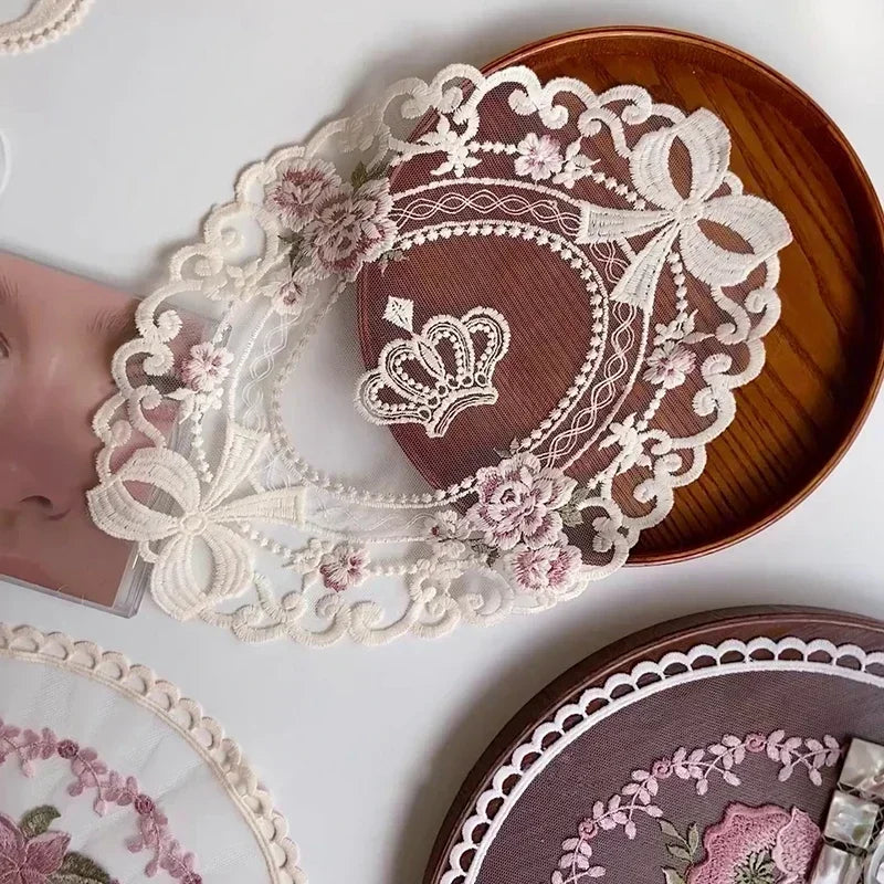 A close-up of an elegant oval lace embroidered placemat with pink floral details on a dark brown wooden plate.