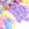 A collection of colorful water-soluble laundry fragrance beads in purple, yellow, and pink are shown in small plastic bags.