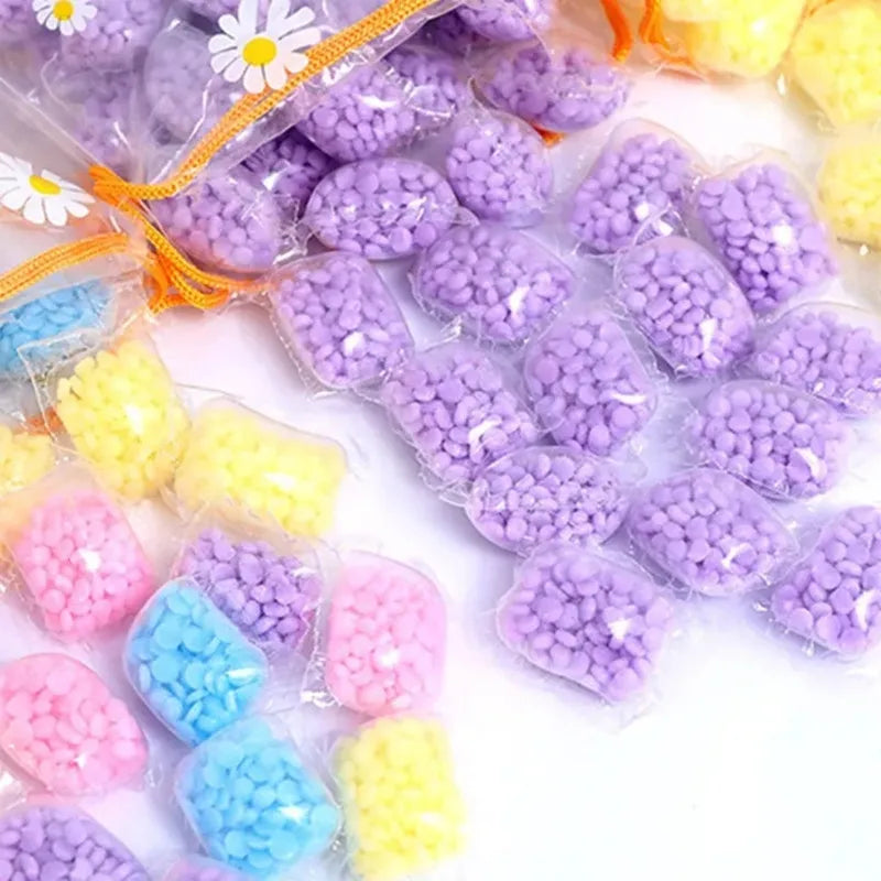 A collection of colorful water-soluble laundry fragrance beads in purple, yellow, and pink are shown in small plastic bags.