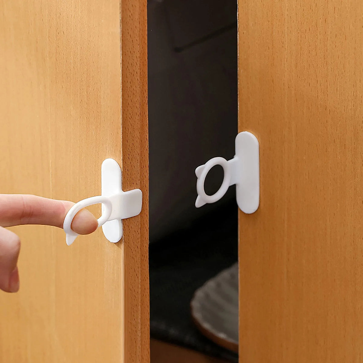A hand is using a white silicone toilet lid lifter with a self-adhesive hook to open a wooden cabinet door.