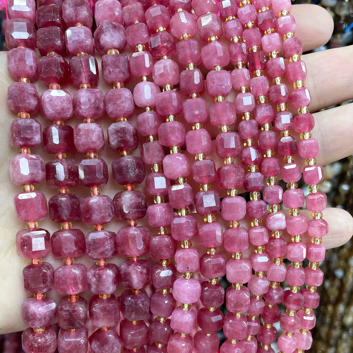 A close-up of pink and reddish rose quartz square faceted beads strung together for jewelry making