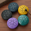 Six colored mini steel tongue drums with mallets arranged in a circle on a wooden surface.