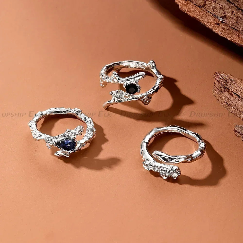 Silver irregular heart-shaped rings featuring dark blue stones displayed on a brown background