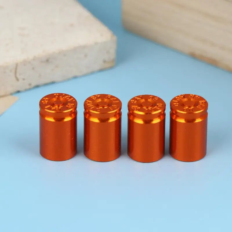 A set of four metallic copper-colored bullet shell tire valve stem caps arranged in a row on a light blue surface.