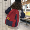 Back view of a red and navy canvas patchwork backpack worn by a person in a modern indoor setting.