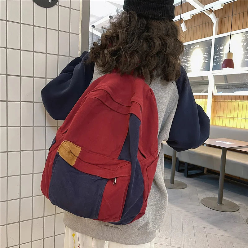 Back view of a red and navy canvas patchwork backpack worn by a person in a modern indoor setting.