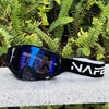 A pair of black HD Motocross goggles with a blue anti-fog lens resting on a light surface.