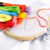 A bamboo embroidery hoop with colored threads and a needle is shown on a white fabric.