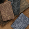 A stack of custom leopard print passport holders in brown and gray tones with personalized embossing.
