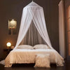 A sheer white ceiling-hung dome mosquito net draped over a bed in a dimly lit room.