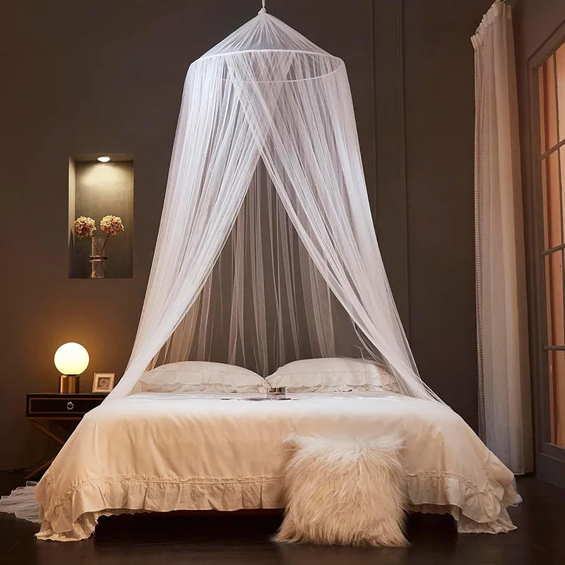 A sheer white ceiling-hung dome mosquito net draped over a bed in a dimly lit room.
