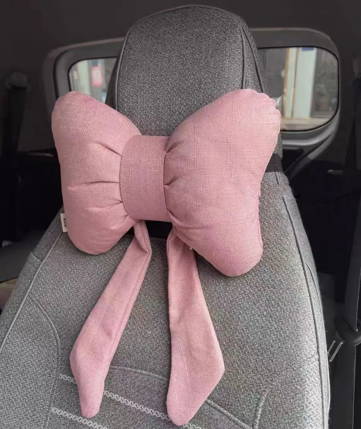 A pink butterfly bow tie neck pillow with a matching fabric cover is shown in a car seat context.
