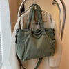 A light beige jacket is displayed on a hanger, featuring a green corduroy tote bag with an adjustable strap.