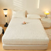 A white fitted sheet is laid on a bed, with a decorative arrangement of dried flowers in the center.