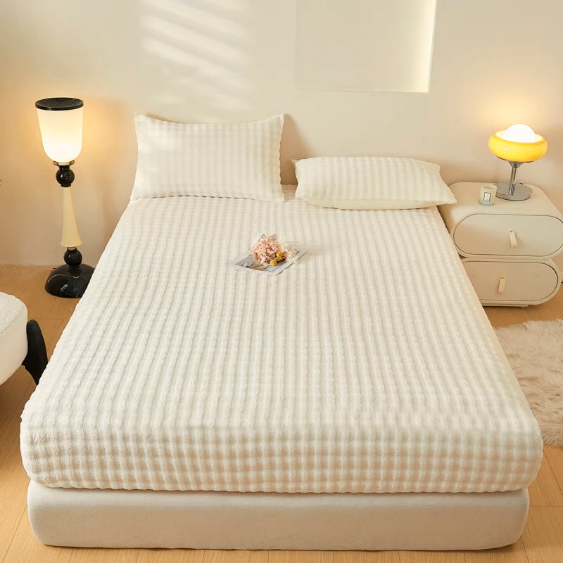 A white fitted sheet is laid on a bed, with a decorative arrangement of dried flowers in the center.