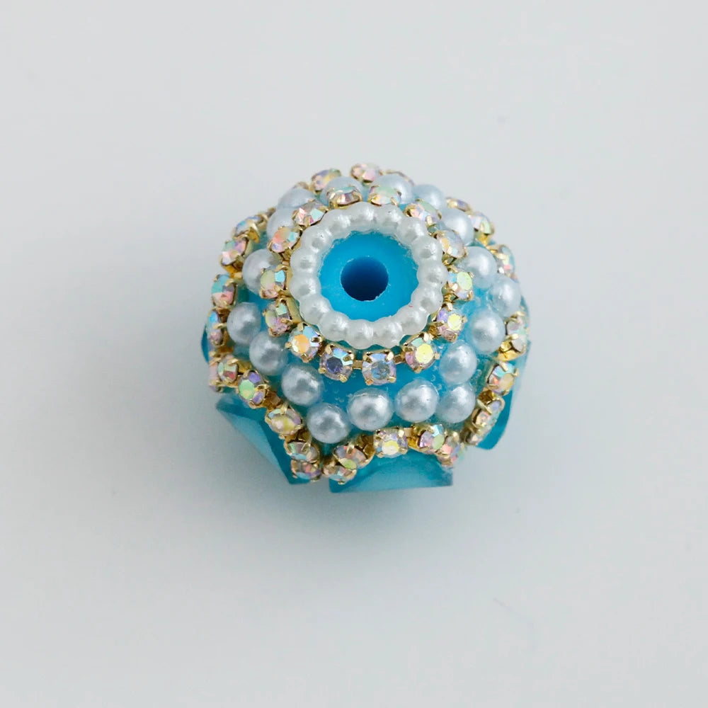 A round, light blue bead embellished with white pearls and gold-toned rhinestones.