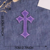 A purple embroidered cross patch on a denim fabric background.