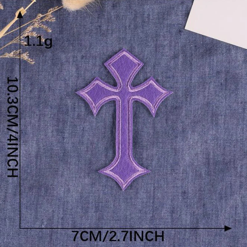A purple embroidered cross patch on a denim fabric background.