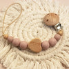 A wooden pacifier clip with crochet beads and a chain rests on a cream-colored crocheted mat.