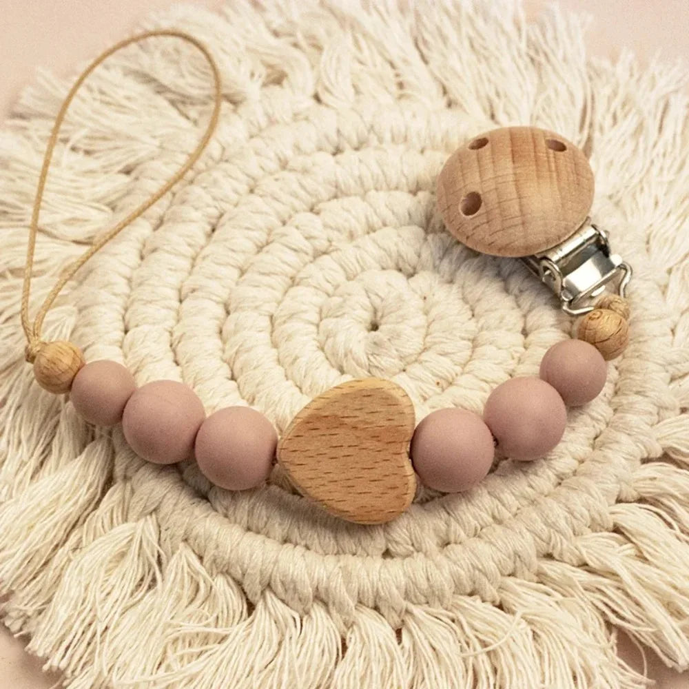 A wooden pacifier clip with crochet beads and a chain rests on a cream-colored crocheted mat.