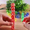 A hand holds a stack of red and white polka-dot acrylic dice on a wooden surface with green foliage in the background.