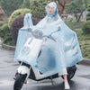 A woman wearing a transparent blue polka-dot waterproof motorcycle rain poncho with a hood, standing next to a white scooter.