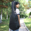 A young man stands outdoors holding a black acoustic guitar soft case with a padded shoulder strap.
