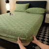 A hand is touching the elastic edge of a green textured mattress cover on a bed.
