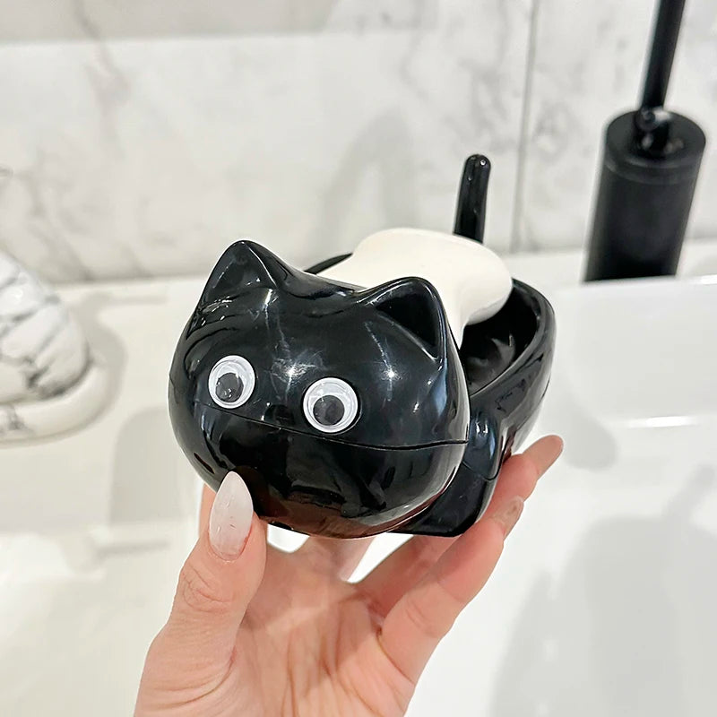 A black cat-shaped soap box with a drainage tray is held in a hand next to a white sink.