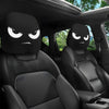 A pair of black car headrest covers with slanted eyes are shown inside a vehicle cabin.