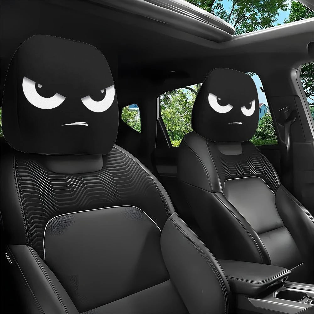A pair of black car headrest covers with slanted eyes are shown inside a vehicle cabin.