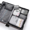 A dark gray travel packing cube case containing six soft laundry pouches for organization.