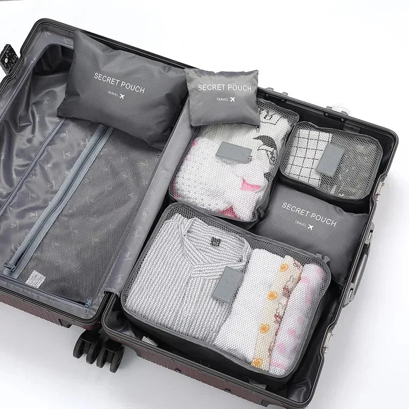 A dark gray travel packing cube case containing six soft laundry pouches for organization.