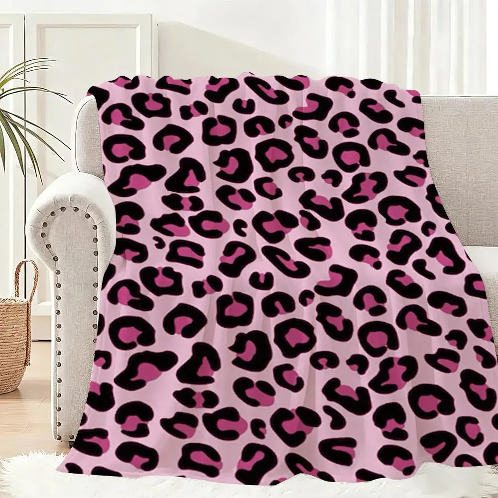 A pink leopard print flannel throw blanket draped over a light-colored sofa.