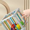 A white rainbow shape sorter cube with colorful elastic bands is shown being held by a hand.