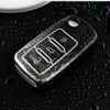 A close-up shot of a silver TPU car key cover resting on a dark, water-beaded surface.