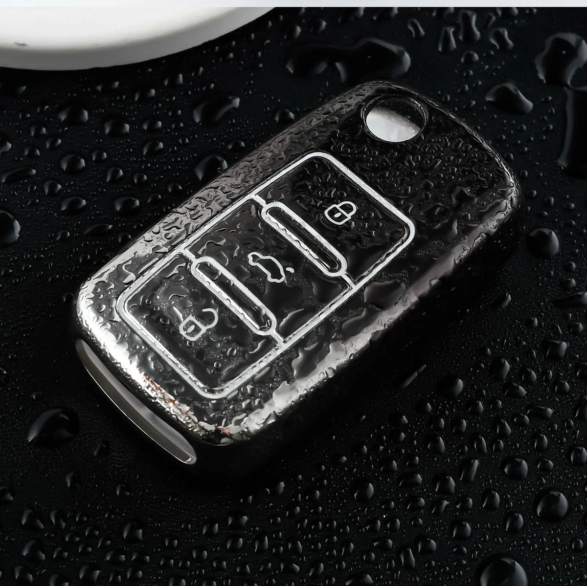 A close-up shot of a silver TPU car key cover resting on a dark, water-beaded surface.