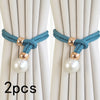 A pair of teal rope curtain tie-backs with gold accents and pearl beads against a light beige curtain.