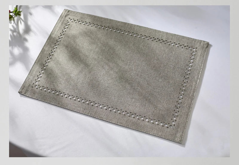 A rectangular linen placemat in a light gray color with decorative stitching is displayed on a white surface.