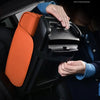 A hand is placing a black car armrest cushion with an orange cover and storage into a vehicle interior.