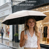 A woman holding a beige umbrella in the rain, demonstrating its dual use for sun and rain protection.