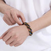 A hand is wearing a chunky stainless steel Cuban chain bracelet with multicolored beads on the wrist.
