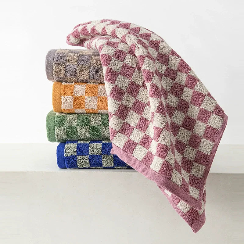 A stack of soft plaid cotton bath towels in various muted colors including purple, beige, green, and blue.