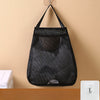 Black mesh wall-mounted garbage bag holder with hooks hanging on a beige wall.