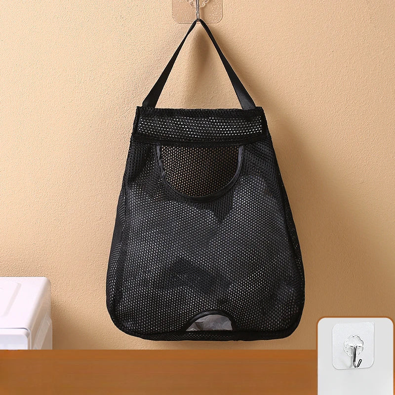 Black mesh wall-mounted garbage bag holder with hooks hanging on a beige wall.