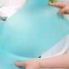 A hand is placing a light blue, textured shelf liner into a white porcelain sink or tub.